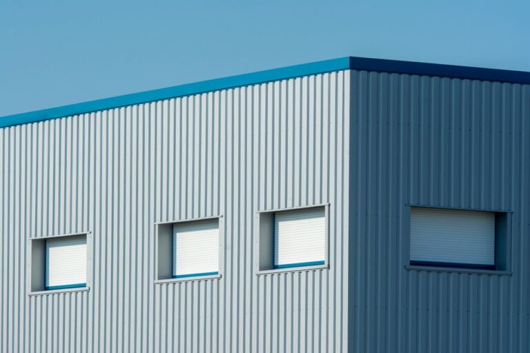 A sleek industrial building with a corrugated metal facade featuring roller blinds and sandwich panels.