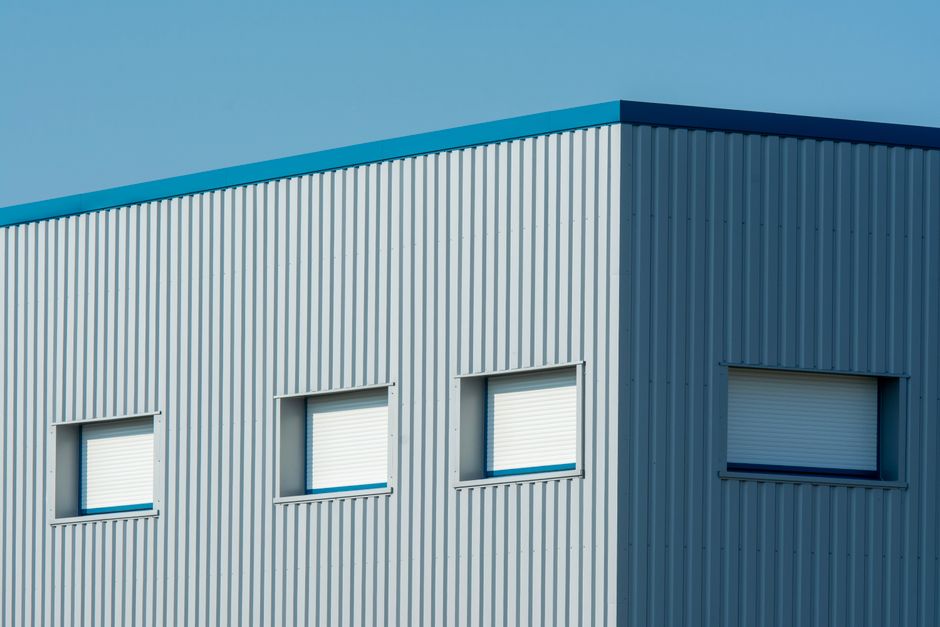A sleek industrial building with a corrugated metal facade featuring roller blinds and sandwich panels.